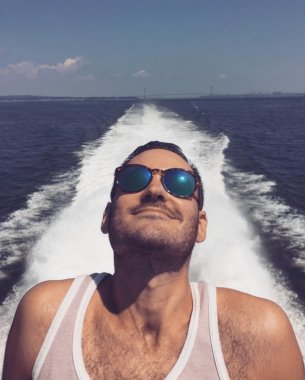 A selfie of a young man on the stern of the boat with the wake in the background