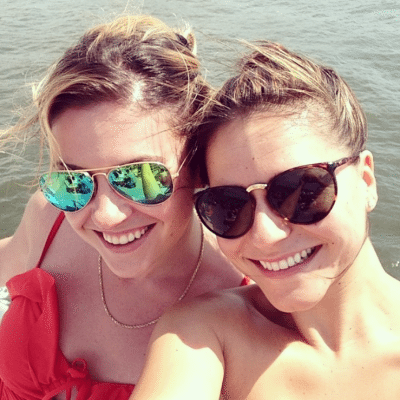 Two young woman wearing sunglasses with the water in the background
