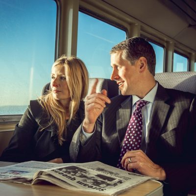A businesswoman and businessman read the newspaper while sitting inside the ferry