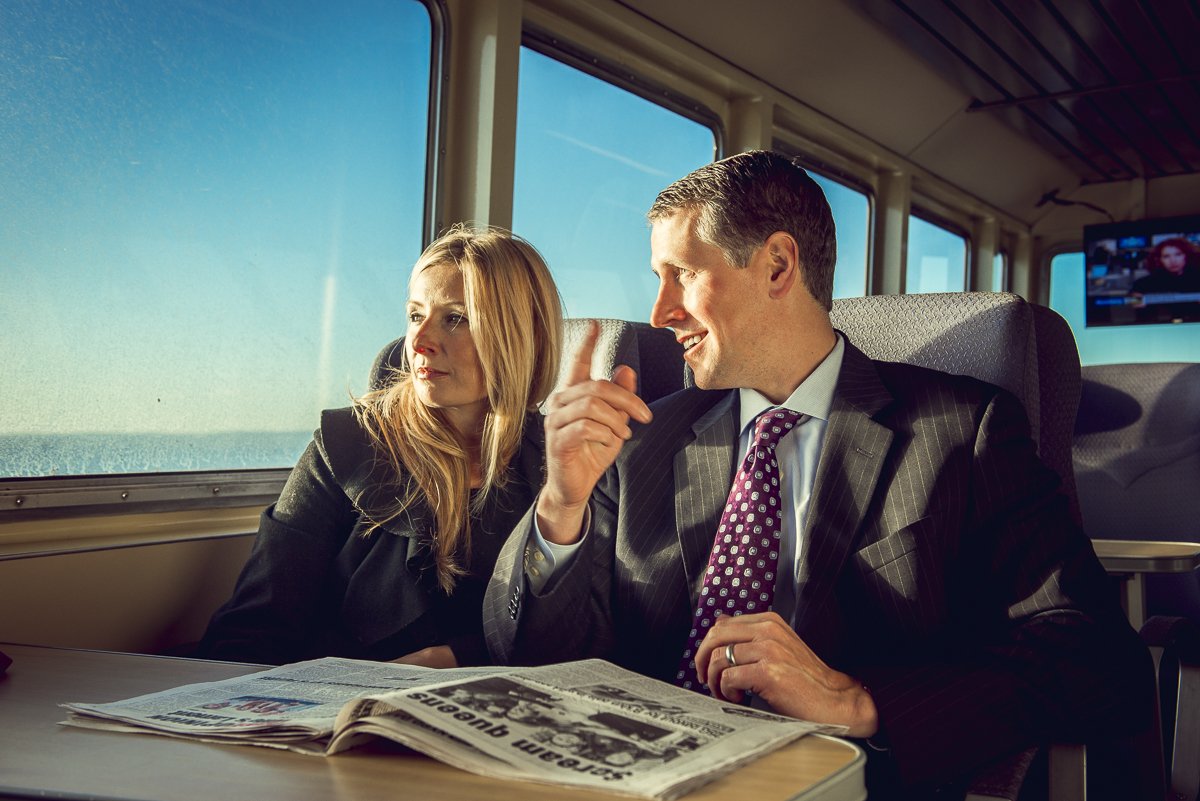 A businesswoman and businessman read the newspaper while sitting inside the ferry
