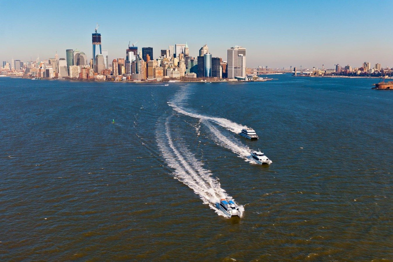 Several Seastreak ferries make their way across the harbor with views of Lower Manhattan in the background