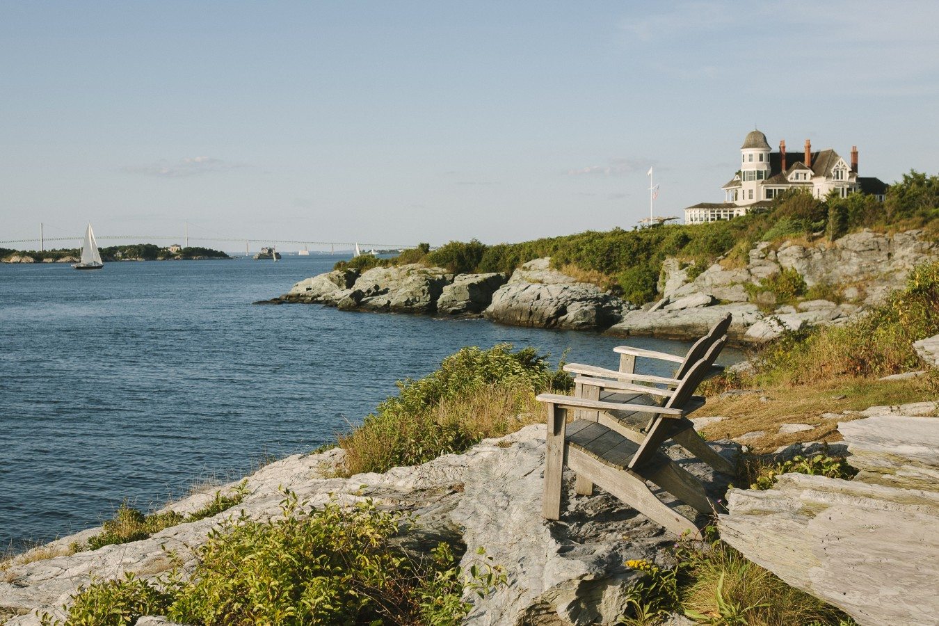 Two Adirondak chairs overlook the water in Newport, Rhode Island on a peaceful evening.